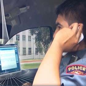 Police officer on cell phone with laptop in police car.